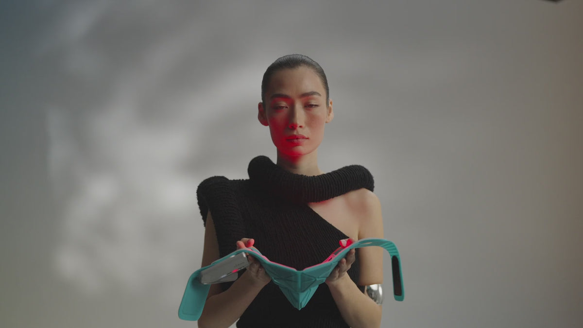 Model lifting the teal Blue Green Mask Lift to her face and putting it on, red light glowing